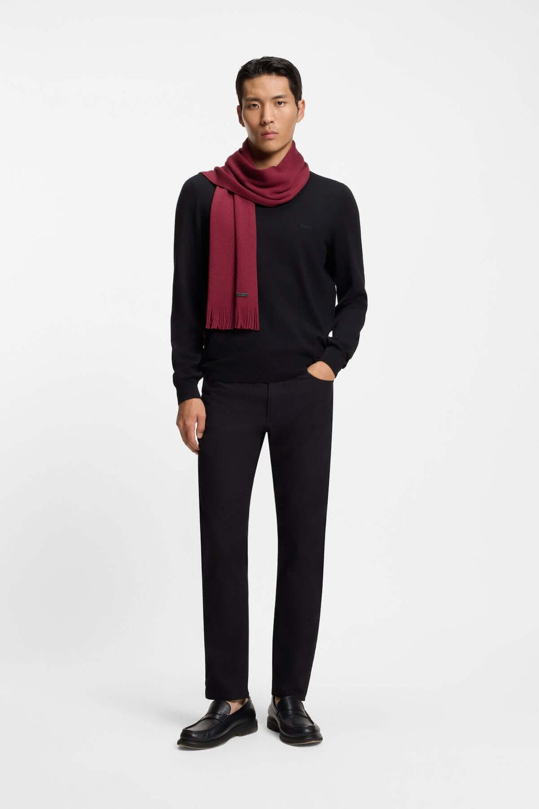 Homme portant le Foulard de laine vierge Boss avec une tenue élégante d'hiver, écharpe rouge sur un pull noir, logo discret visible.