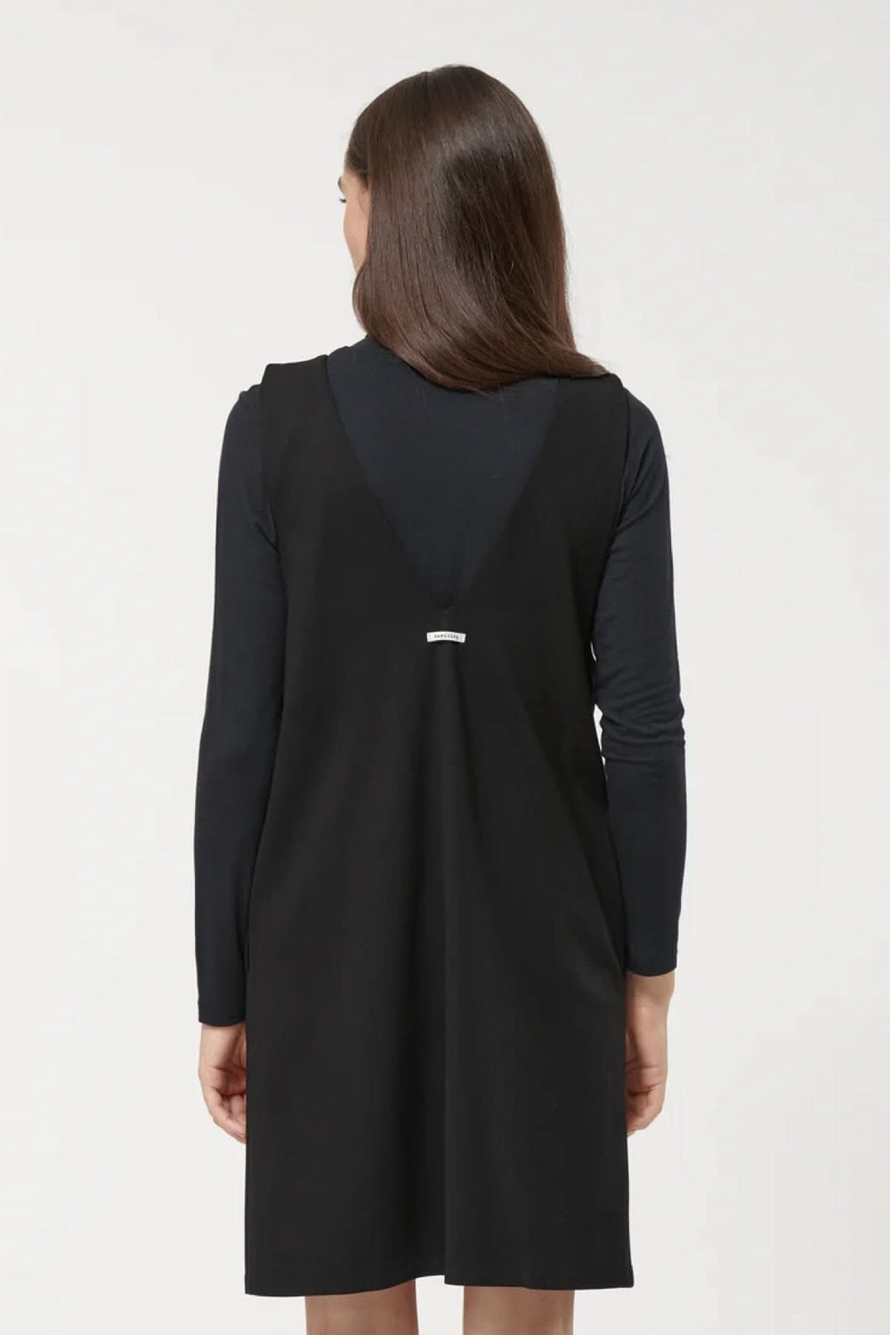 Femme portant une robe sans manches noire à encolure en V, coupe trapèze, sur un sous-pull noir.