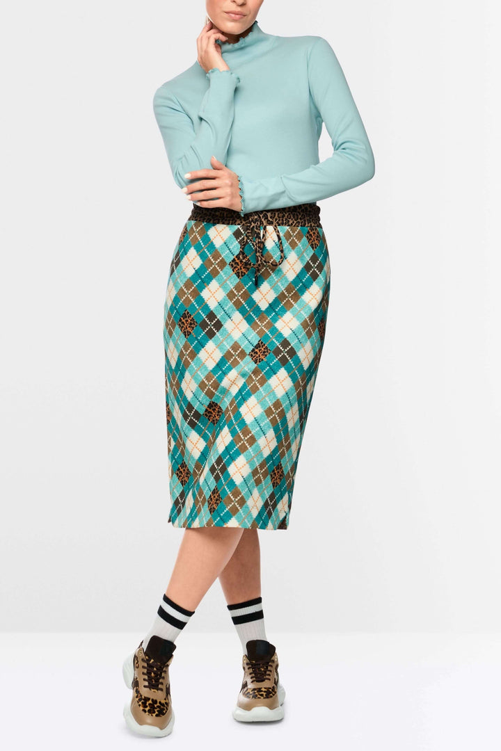 Chandail à col montant et bordures ondulées, style féminin et délicat, porté avec une jupe à carreaux colorés et chaussures tendance.