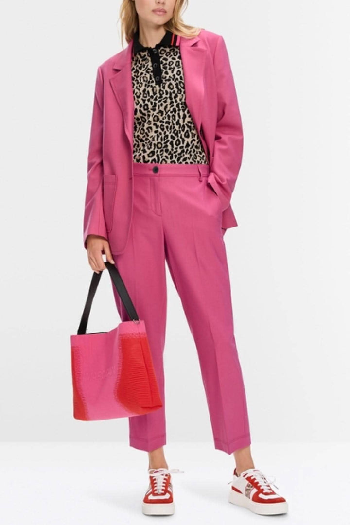 Femme en costume rose vif avec haut en léopard et sac à main, style chic et moderne.