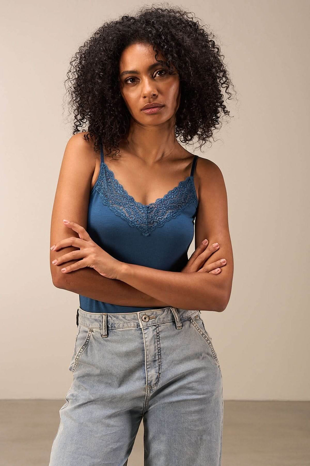 Camisole en dentelle bleu avec fines bretelles, associée à un jean décontracté, style élégant et moderne.