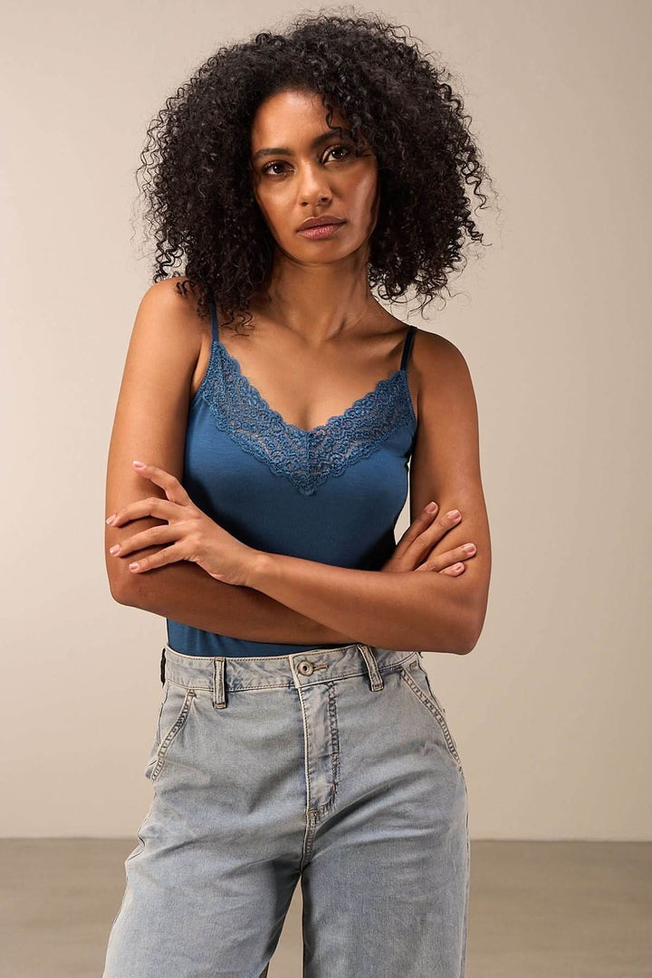 Camisole en dentelle bleu avec fines bretelles, associée à un jean décontracté, style élégant et moderne.