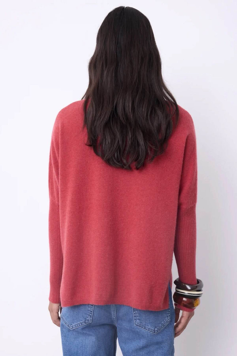 Dos d'une femme portant un chandail à col roulé rouge en cachemire, coupe ample, avec des bracelets et un jean, chic et confortable.