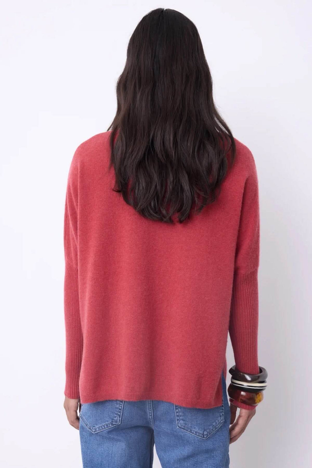 Dos d'une femme portant un chandail à col roulé rouge en cachemire, coupe ample, avec des bracelets et un jean, chic et confortable.