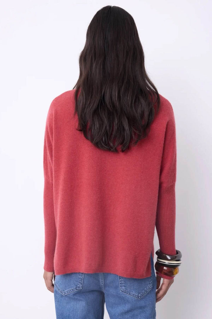 Dos d'une femme portant un chandail à col roulé rouge en cachemire, coupe ample, avec des bracelets et un jean, chic et confortable.