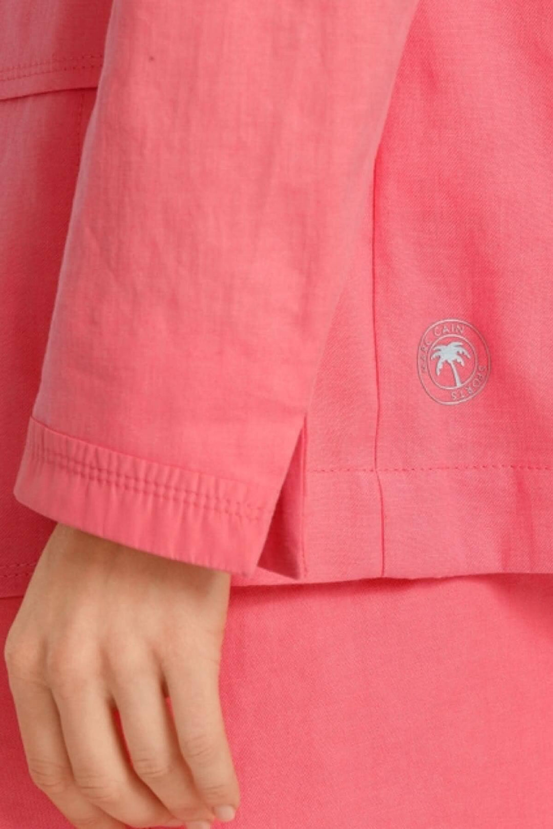 Détail d'un blazer en lin rose avec logo, manches légèrement froissées, idéal pour un look décontracté.