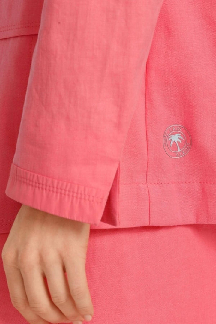Détail d'un blazer en lin rose avec logo, manches légèrement froissées, idéal pour un look décontracté.