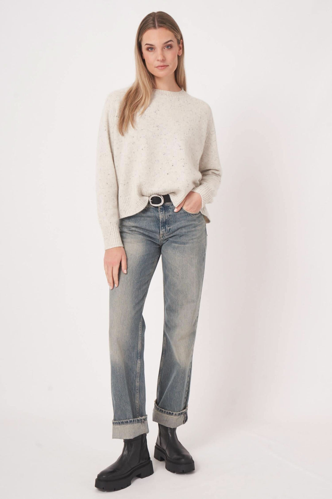 Femme portant un chandail moucheté en cachemire, jean délavé, et bottes noires, style décontracté et élégant.