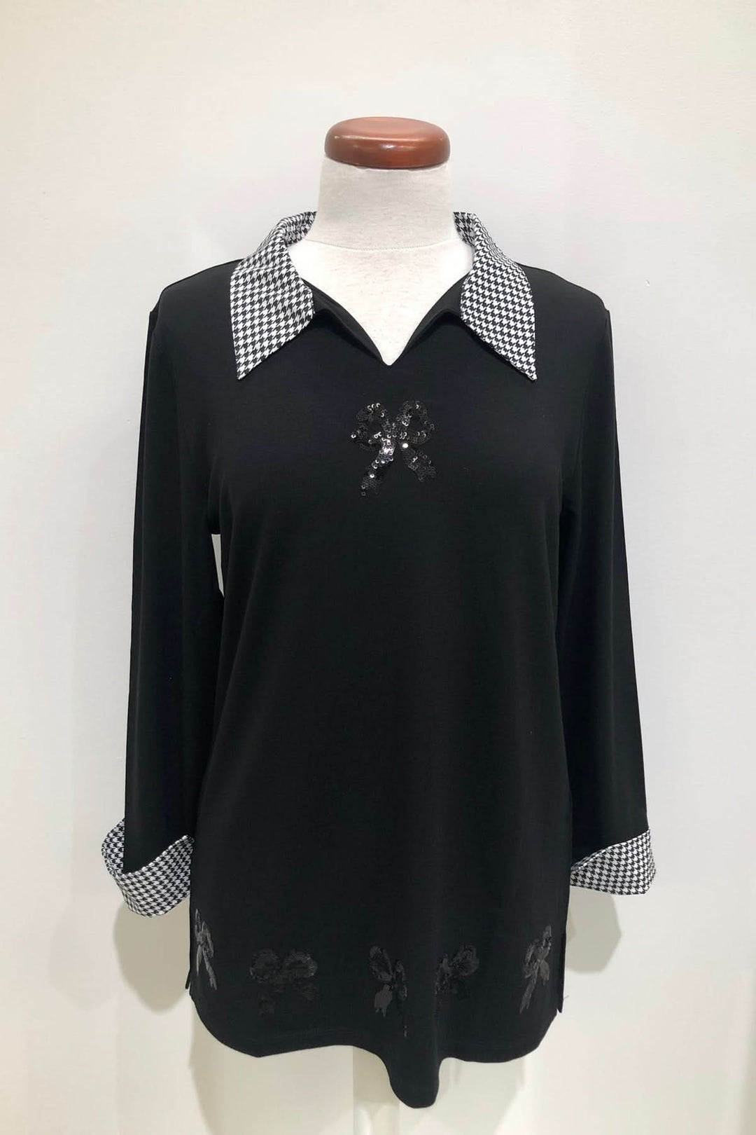 Tunique col chemisier noir avec motifs floraux et poignets à carreaux, élégante et graphique.