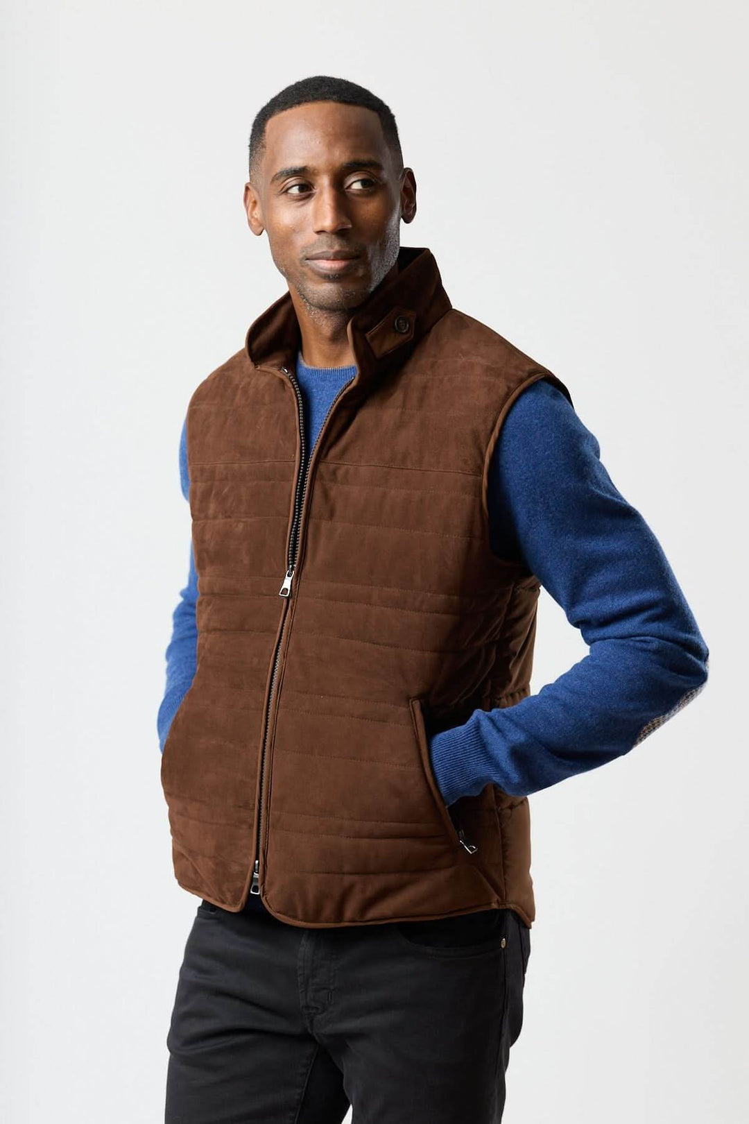 Homme portant une veste sans manches en simili suède marron avec chandail bleu dessous, tenue élégante et contemporaine.