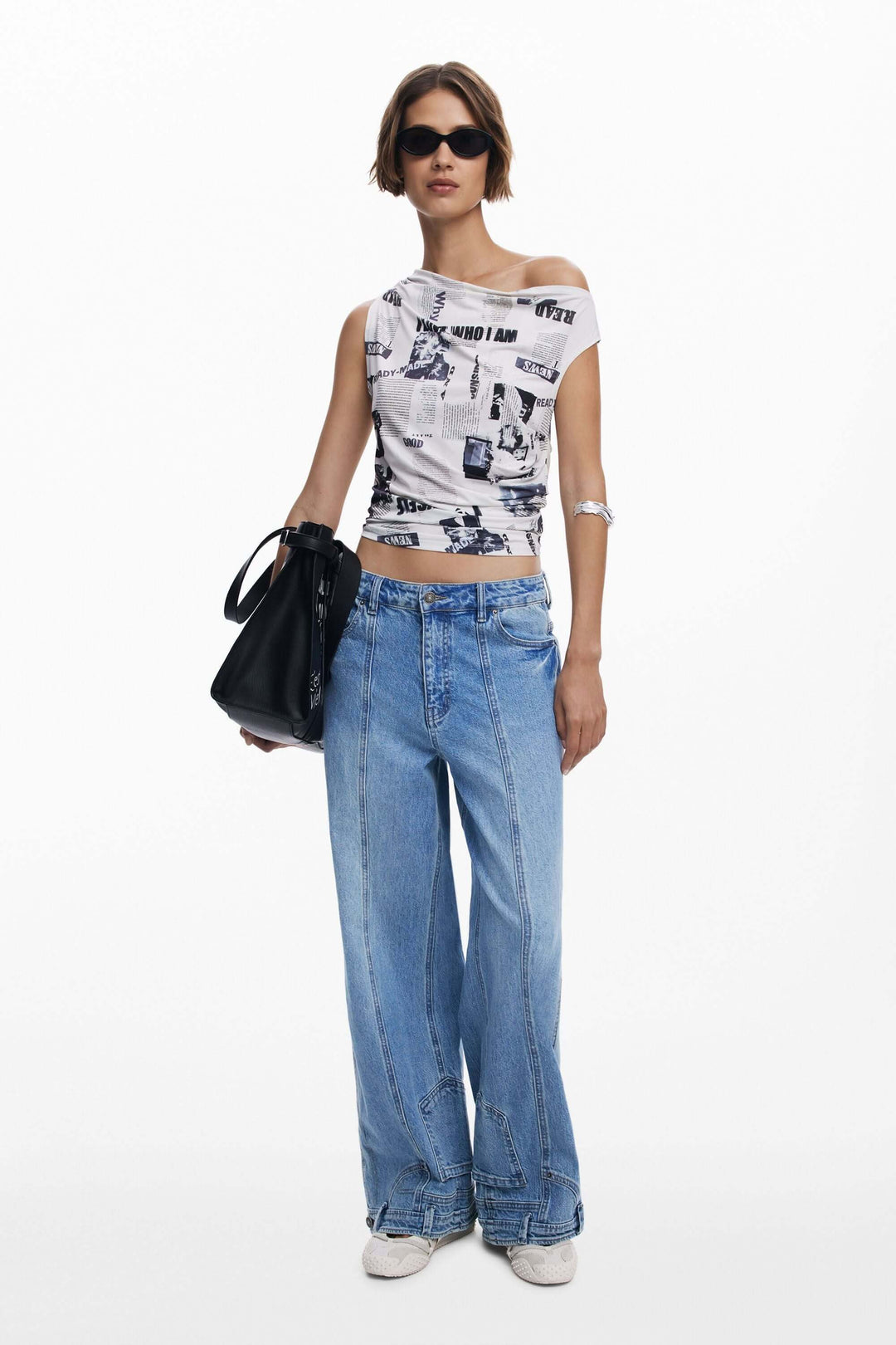 Femme en t-shirt drapé asymétrique avec imprimé typographique, jeans larges et sac noir.