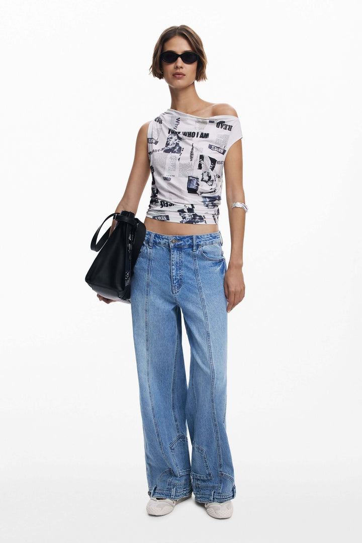 Femme en t-shirt drapé asymétrique avec imprimé typographique, jeans larges et sac noir.