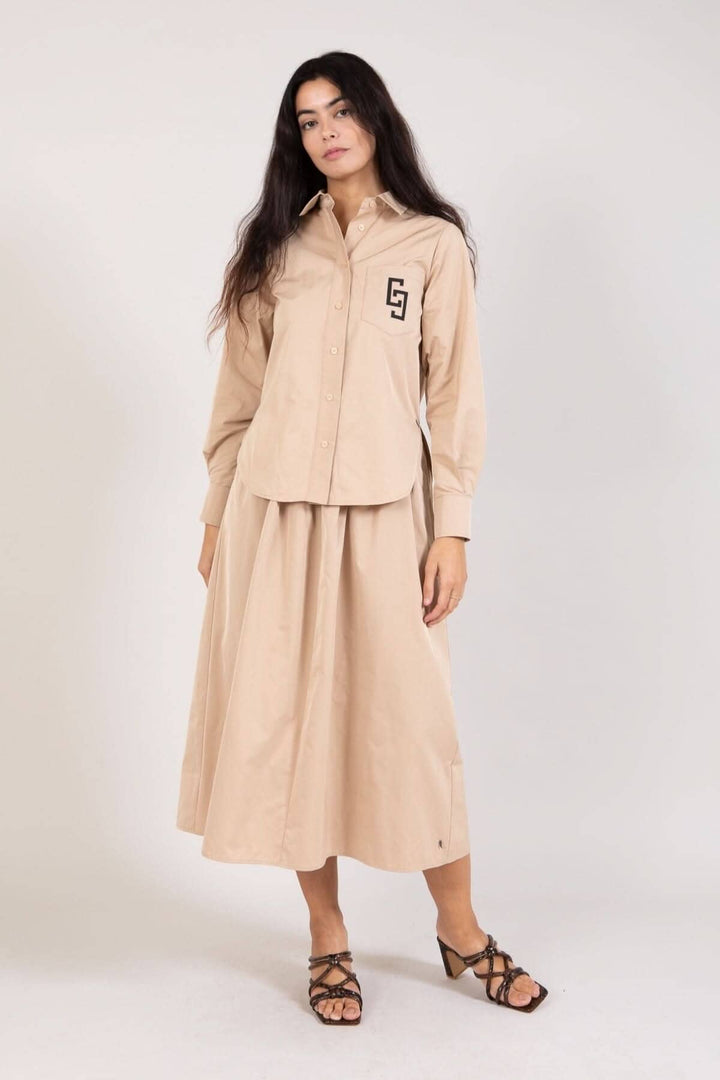 Femme portant une jupe longue beige avec plis et chemise assortie, look élégant et décontracté.