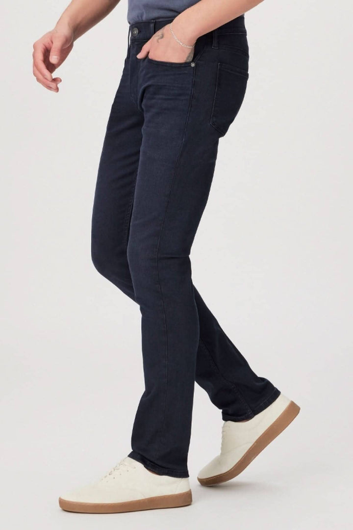 Homme portant des jeans slim délavés foncés en denim TRANSCEND avec des sneakers blanches.