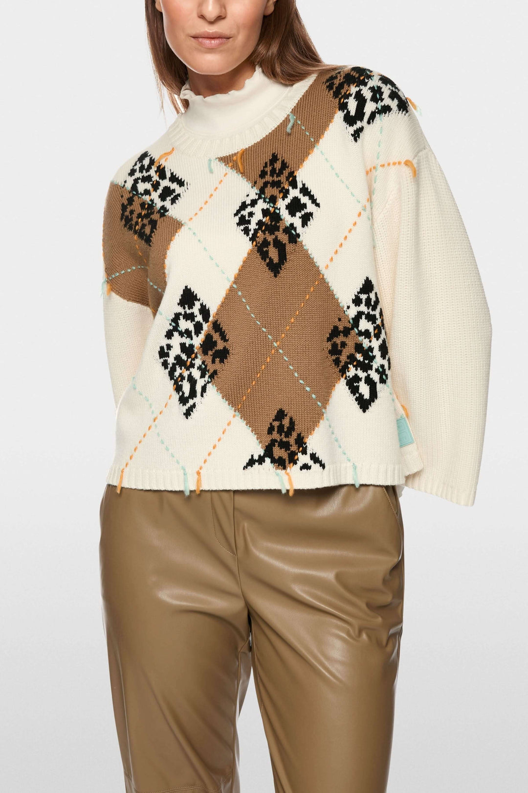 Chandail à motif losanges et accents léopard porté par une femme, coupe ample et col rond, sur fond blanc.