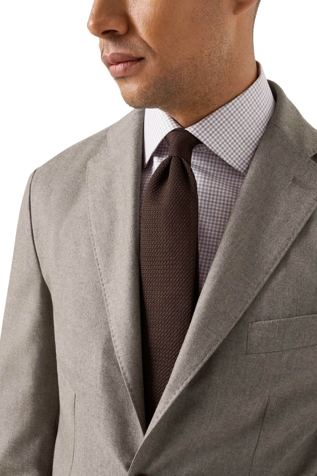Homme portant une chemise en coton à carreaux fins multicolores sous une veste grise, avec cravate marron élégante.