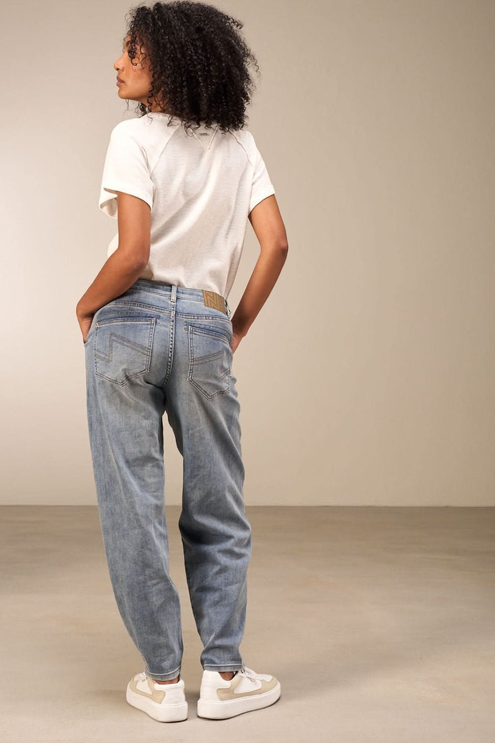 Femme vue de dos portant un jean coupe droite, t-shirt blanc et baskets, dans un cadre minimaliste.