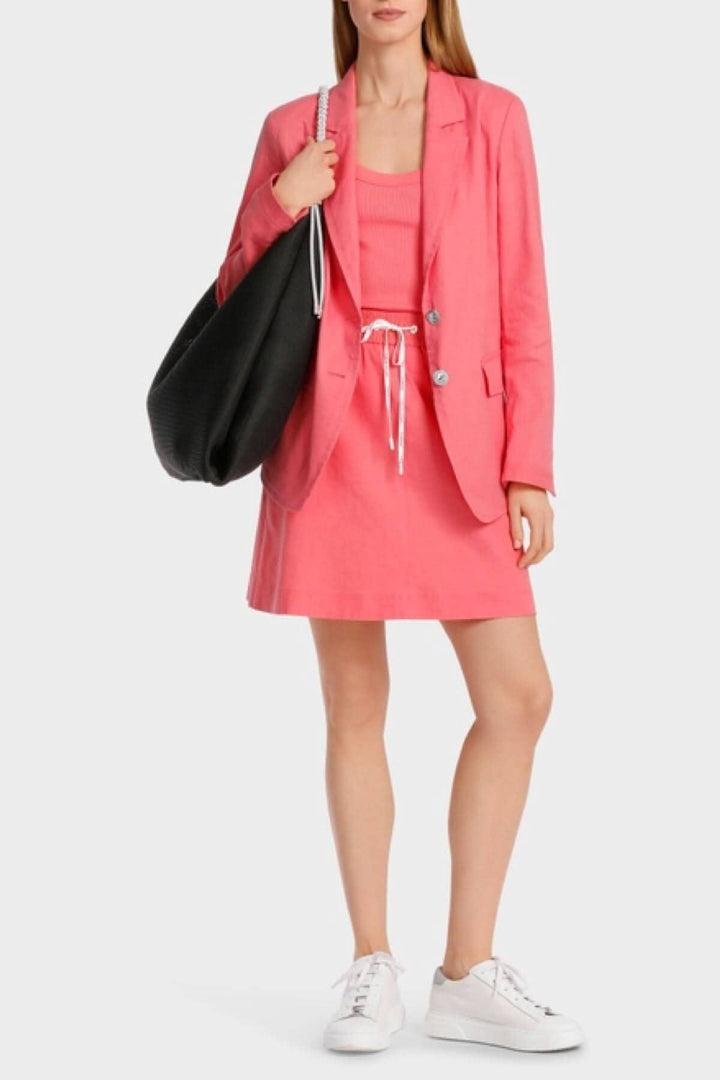 Femme moderne portant un blazer en lin rose sur une robe décontractée avec un sac noir.