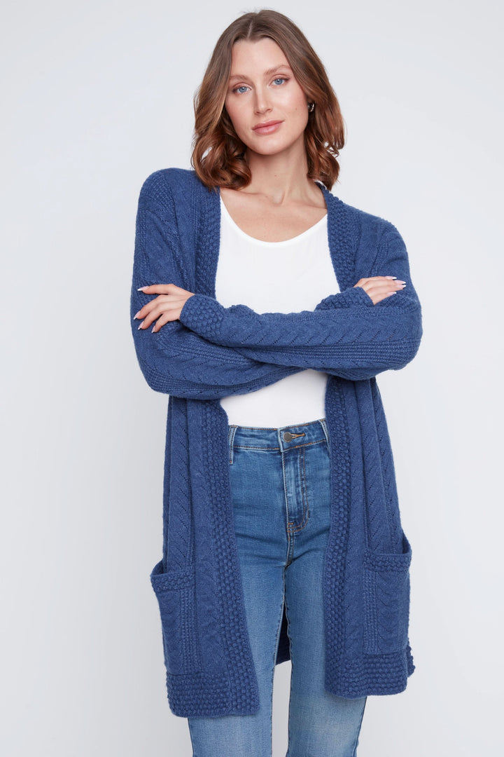 Cardigan long à maille torsadée bleu avec poches, porté sur un haut blanc et jean.