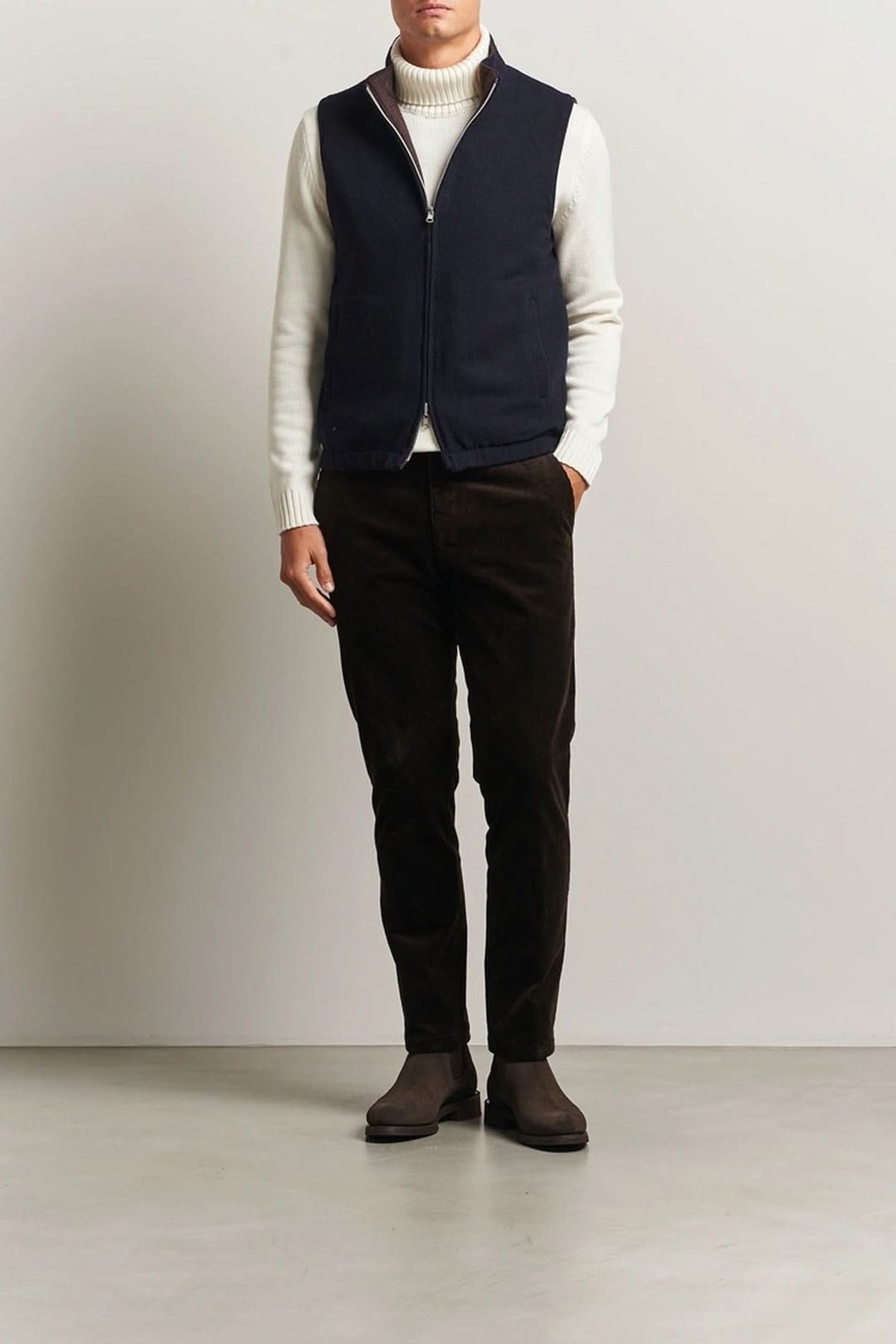 Homme portant un gilet en laine reversible avec un col roulé blanc et un pantalon noir, style élégant et raffiné.