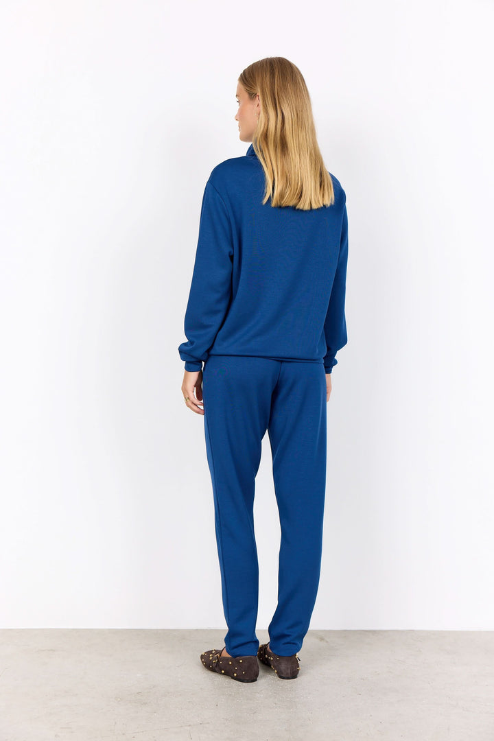 Femme vue de dos portant un chandail col montant bleu et un pantalon assorti, dans un style décontracté.