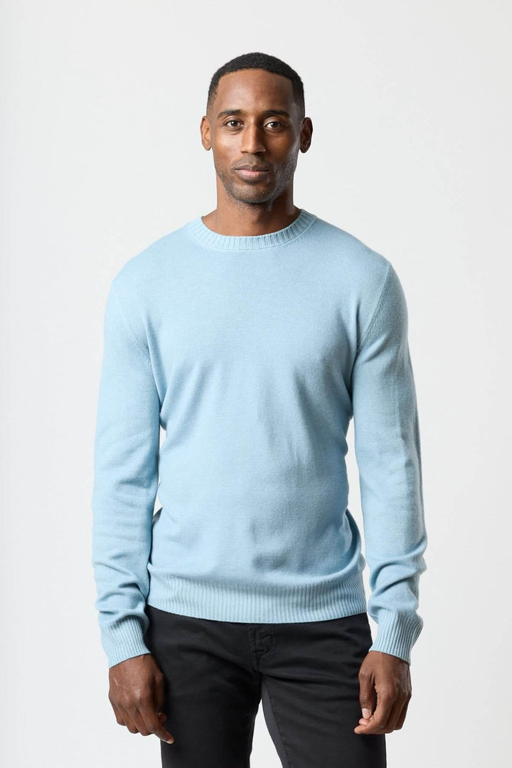 Homme portant un chandail col rond en maille douce bleu clair avec un jean noir, look moderne et confortable.