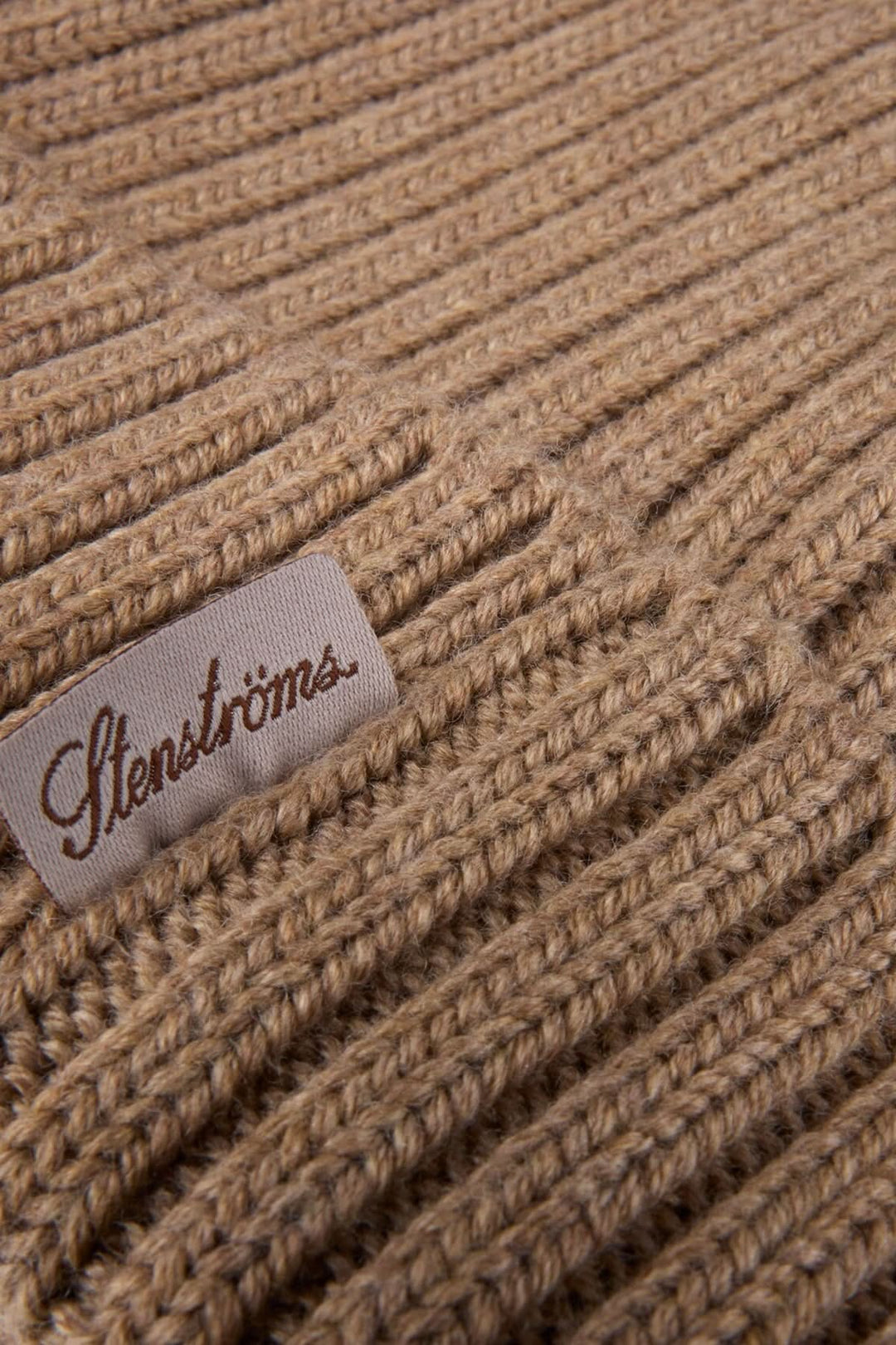 Gros plan sur une tuque en laine mérinos côtelée beige avec une étiquette de marque. Tricot chaud, extensible et élégant.