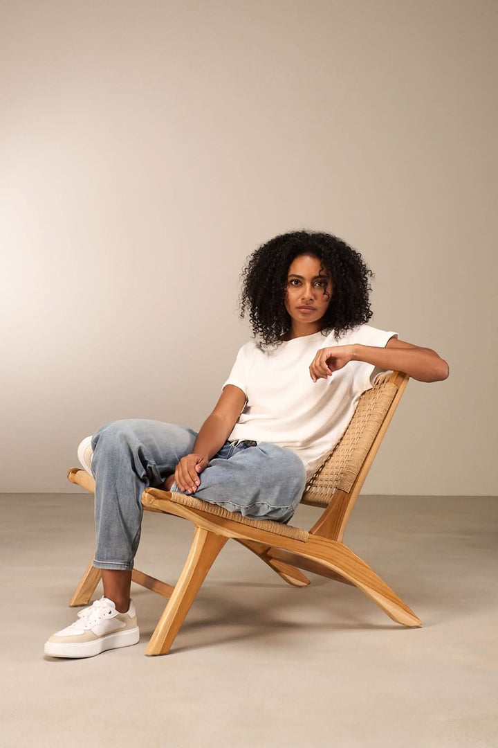 Femme assise sur une chaise en bois, portant un t-shirt blanc et un jean délavé, style décontracté.