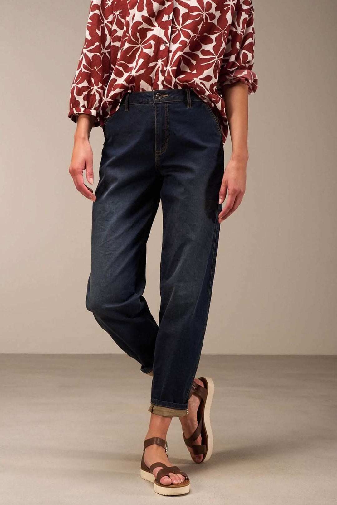 Jean à coupe décontractée denim foncé avec revers, porté avec un chemisier à fleurs et des sandales.