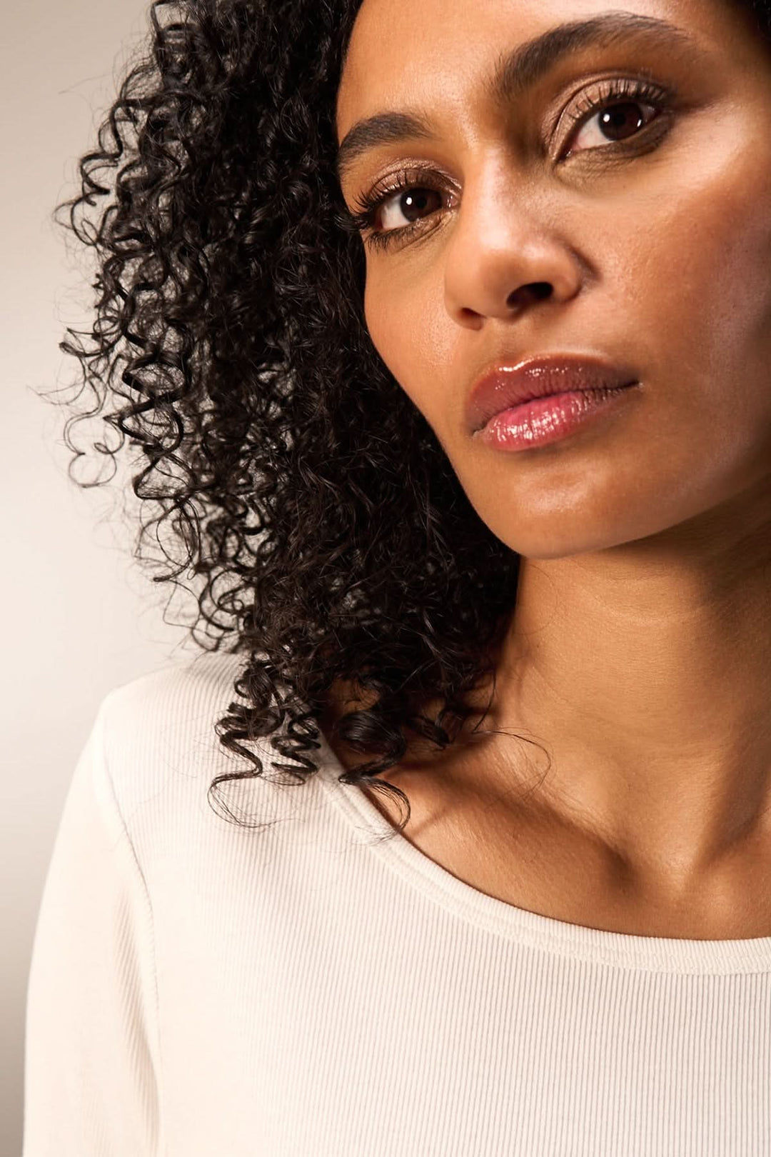 Femme avec cheveux bouclés portant un chandail minimaliste, mettant en avant une allure simple et élégante.