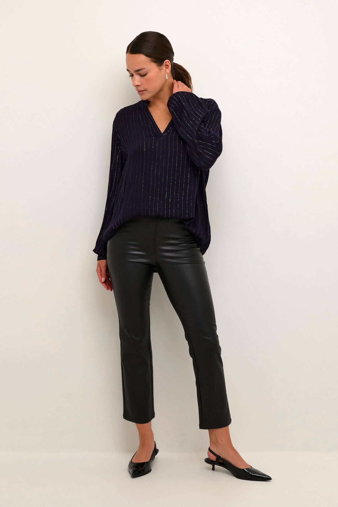 Femme en pantalon noir en simili cuir, coupe ajustée, haut chic rayé et chaussures à talons, look sophistiqué