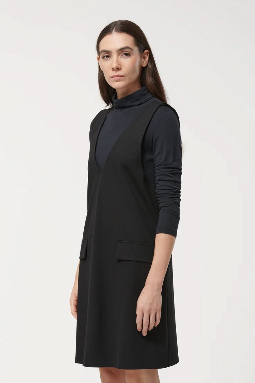 Femme portant une robe sans manches noire, coupe évasée, encolure en V, poches plaquées, style chic et minimaliste.