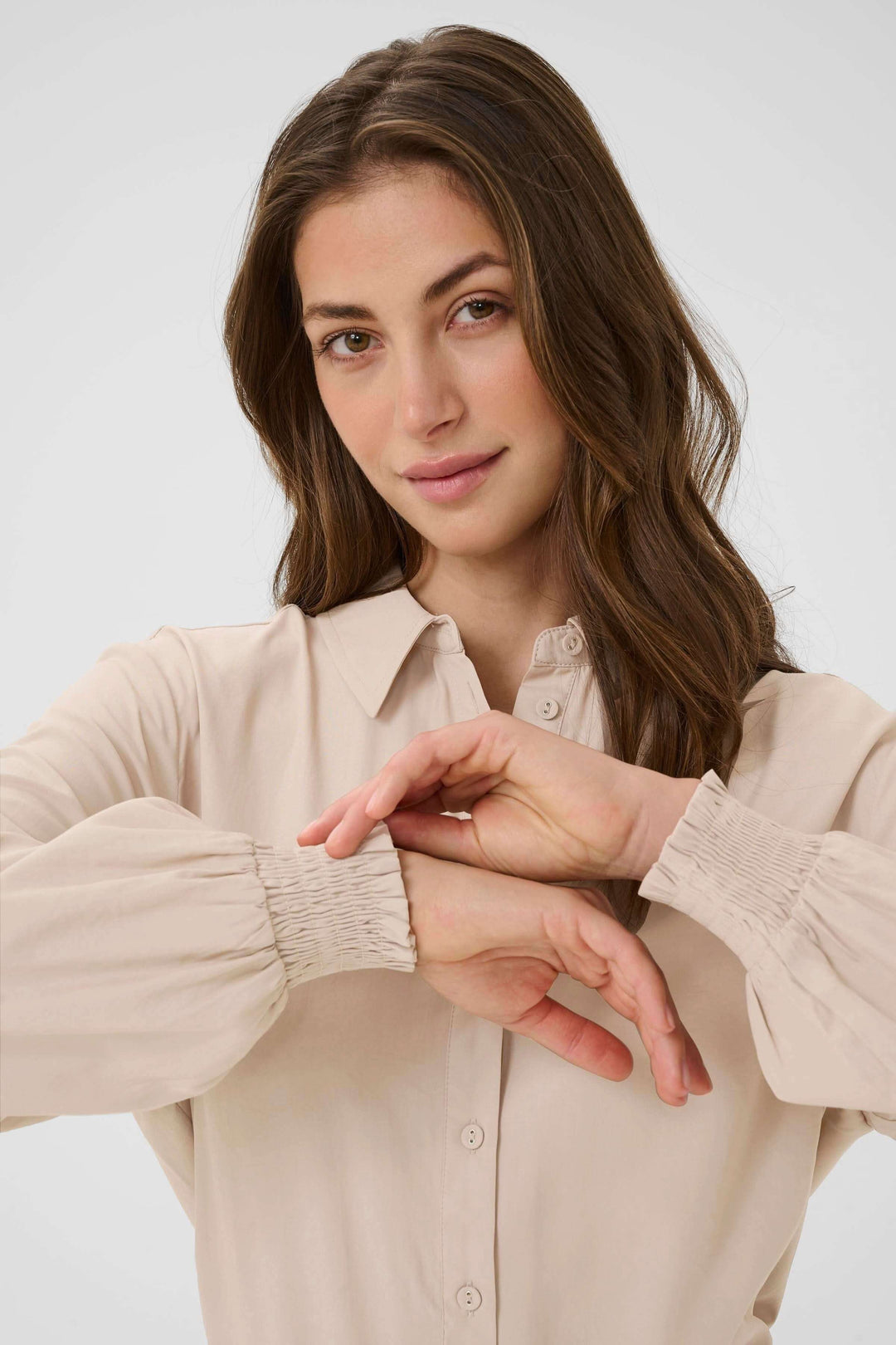 Femme portant une Blouse Nola fluide à poignets smockés en beige, élégante et confortable pour le quotidien.