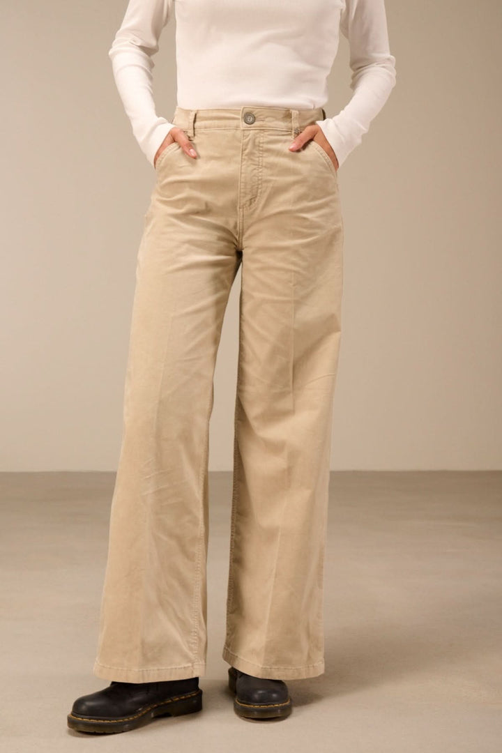 Pantalon large taille haute beige porté par un mannequin, avec poches latérales et taille haute. Idéal pour un look moderne.