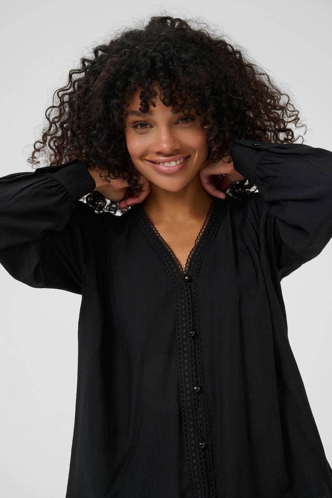 Model wearing Chemise Mirabel à col V et détails de dentelle, showcasing V-neck with lace trim and long puff sleeves in black.