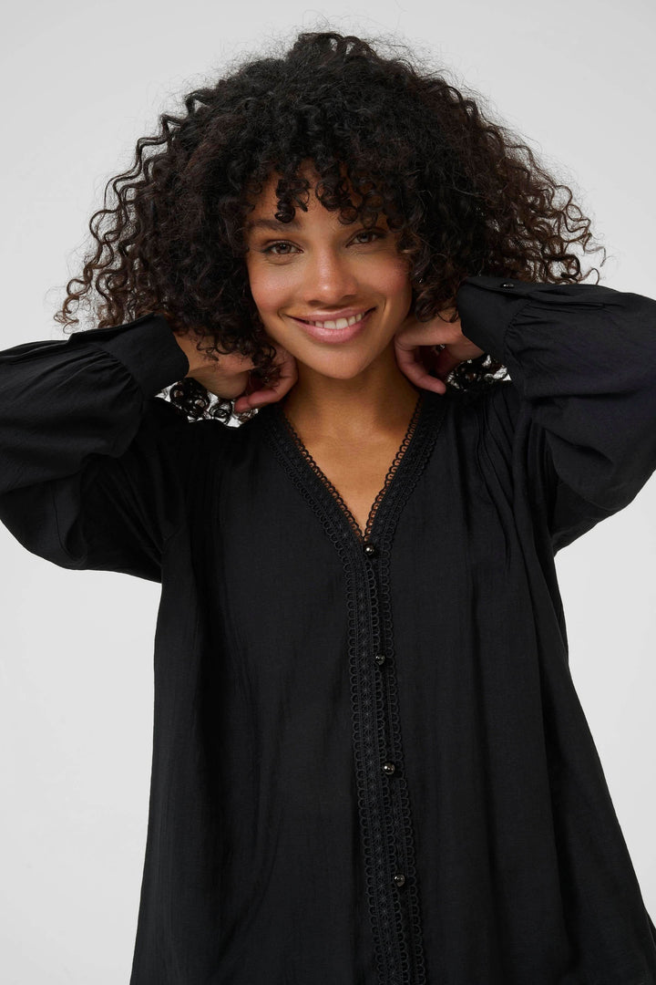 Model wearing Chemise Mirabel à col V et détails de dentelle, showcasing V-neck with lace trim and long puff sleeves in black.
