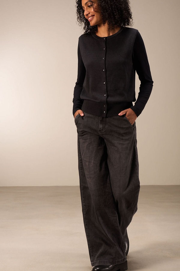 Femme souriante portant un cardigan noir et un jean large, ajoutant confort et style à sa tenue.