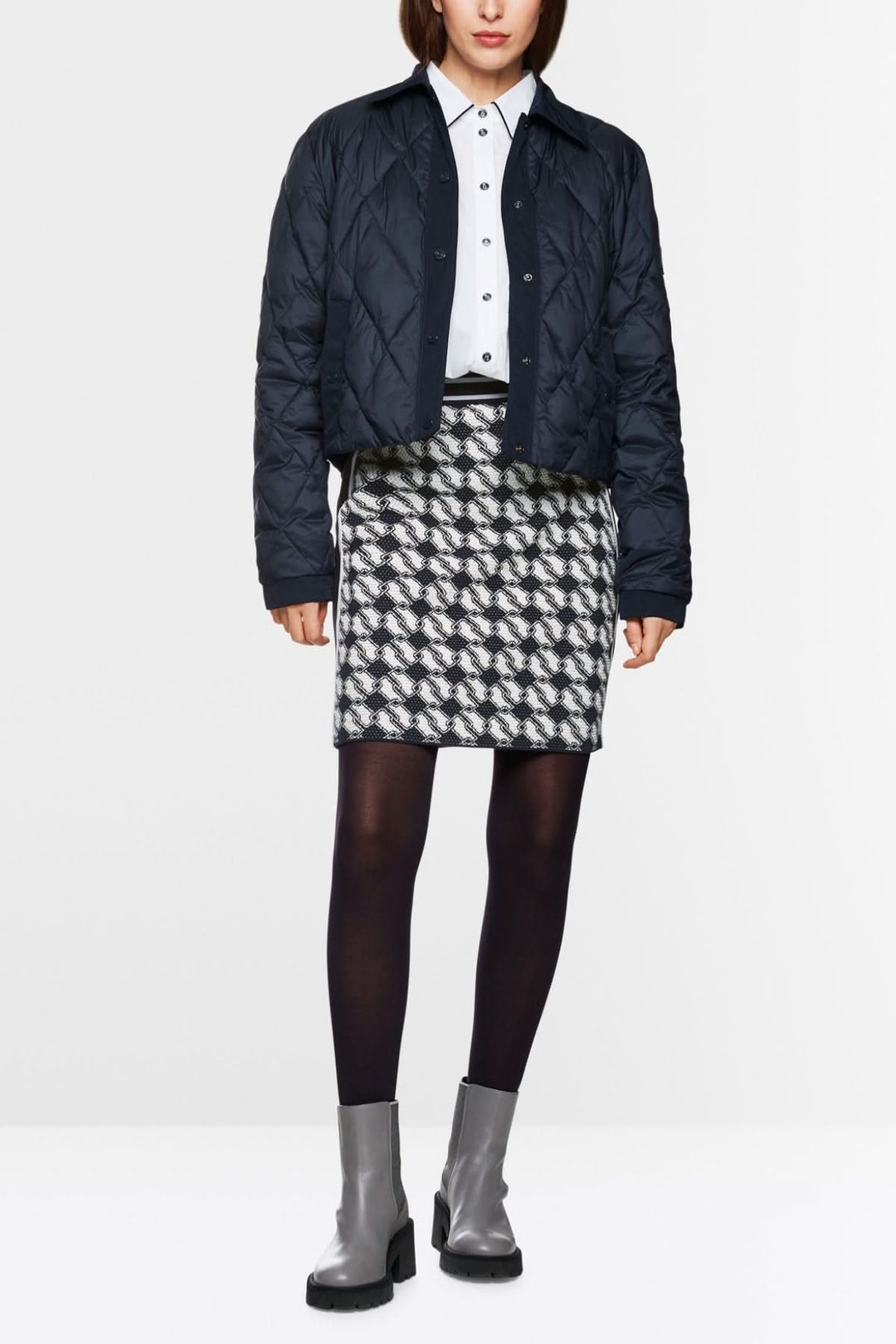 Femme portant une jupe en maille à motif cubique, chemise blanche et veste matelassée, style graphique et moderne.