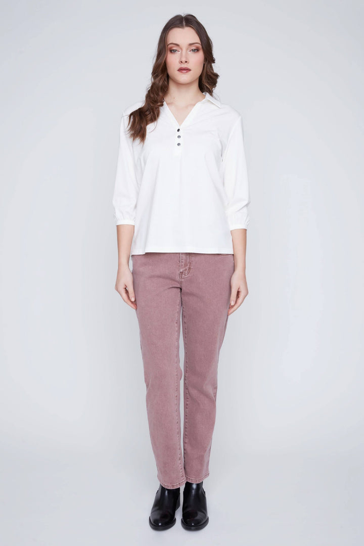 Blouse blanche à manches 3/4 avec encolure en V et patte de boutonnage, portée avec un pantalon rose.