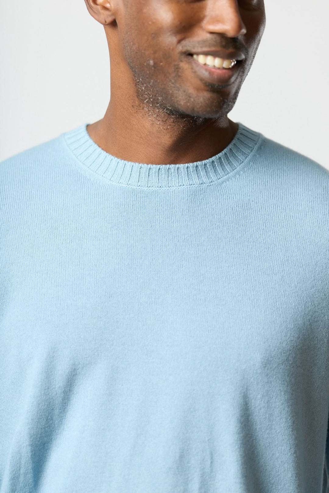 Homme portant un chandail col rond en maille douce bleu, style moderne avec ourlets côtelés.