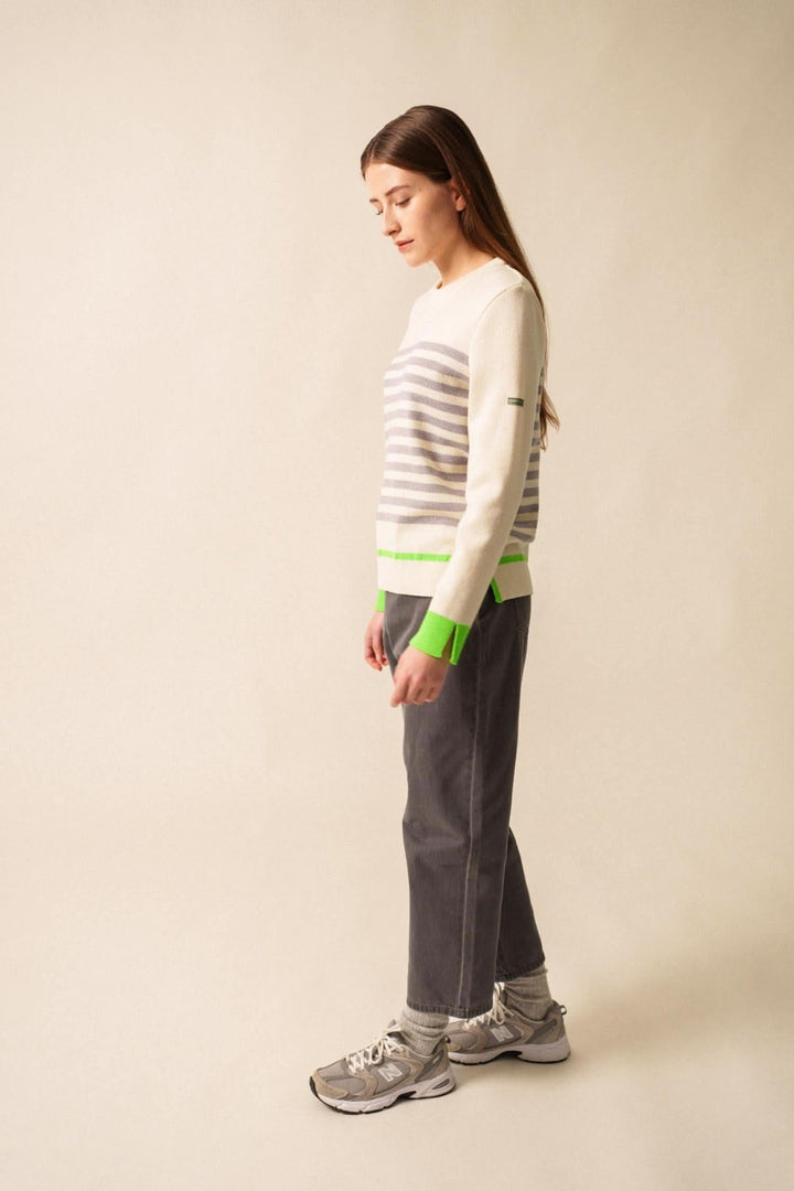 Chandail rayé Evian avec contrastes fluo, porté avec un pantalon gris, look décontracté et moderne.