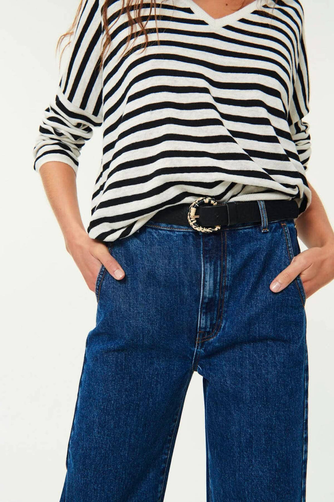 Modèle portant une ceinture Malvina en cuir noir avec boucle en raphia, associée à un pull rayé et un jean.