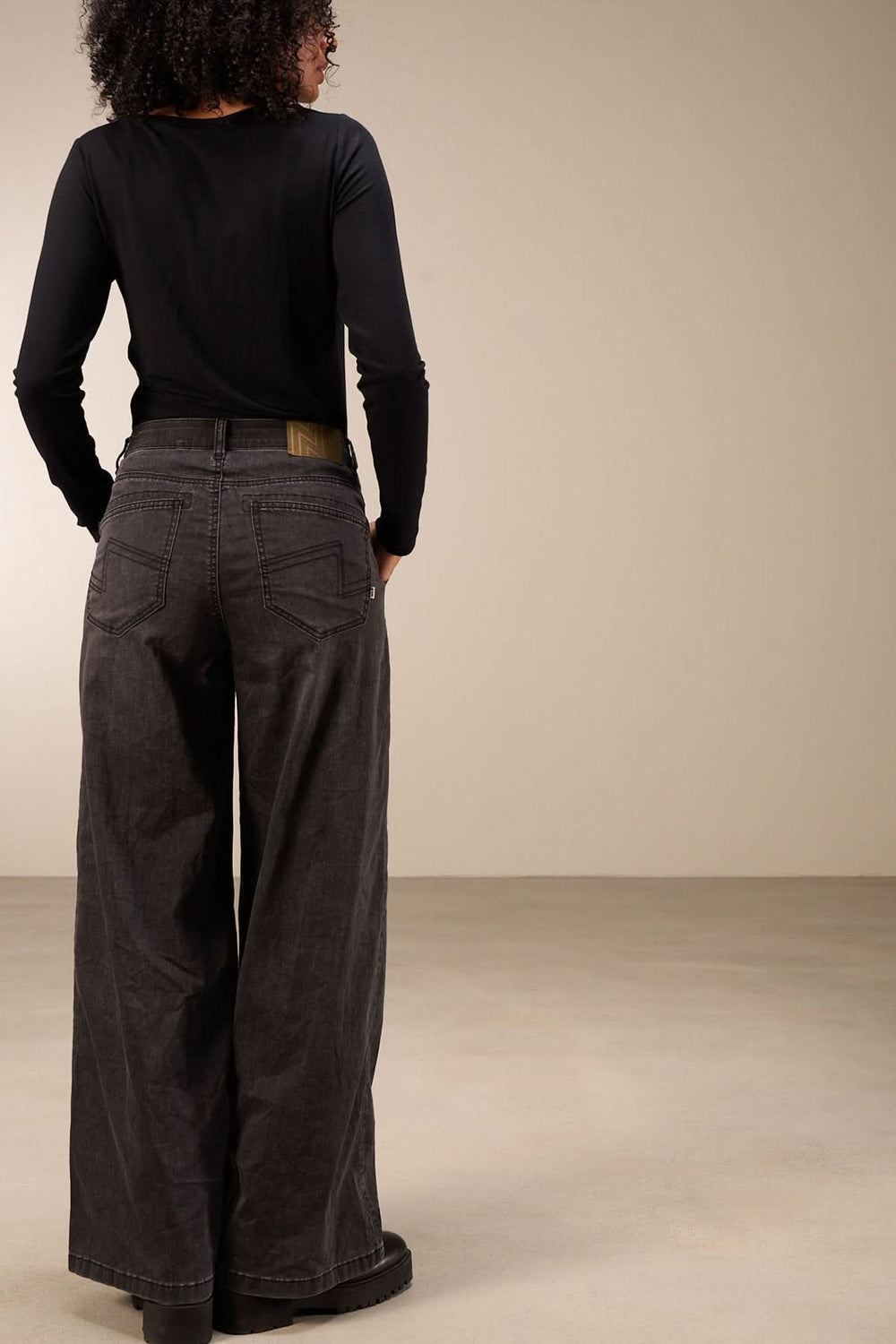 Jean à coupe large, taille mi-haute, vue de dos, porté avec un haut noir. Confort et style décontracté.