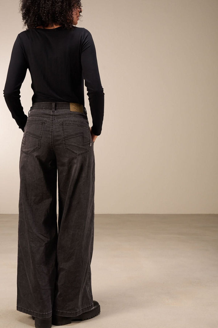 Jean à coupe large, taille mi-haute, vue de dos, porté avec un haut noir. Confort et style décontracté.