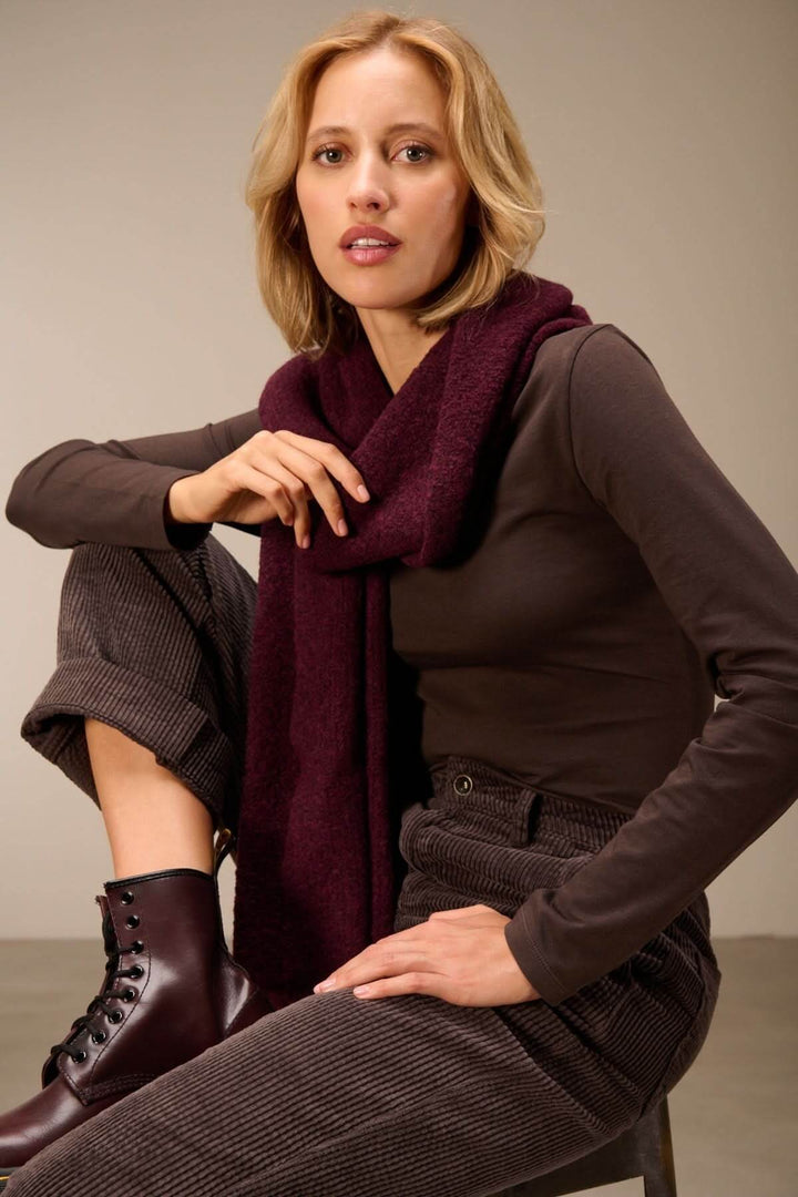 Femme portant un T-shirt manches longues col rond — jersey doux extensible, avec une écharpe bordeaux et un pantalon en velours côtelé marron.