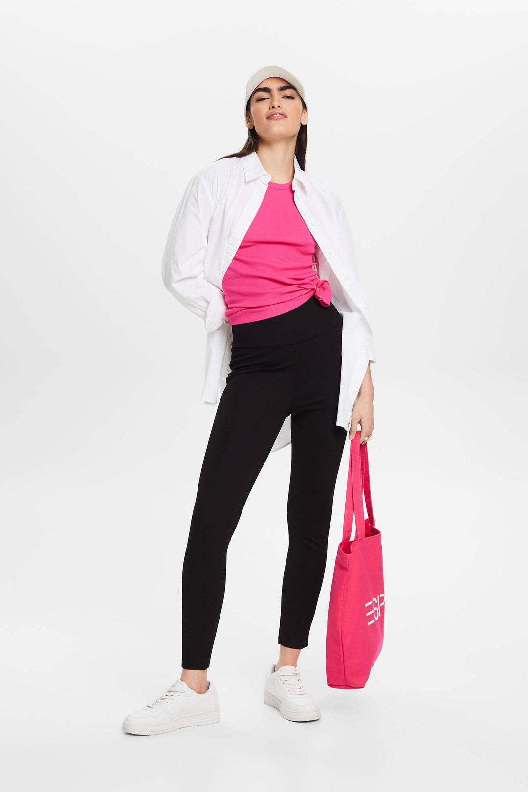 Femme en leggings noirs avec un haut rose et une chemise blanche, tenant un sac rose, style décontracté.