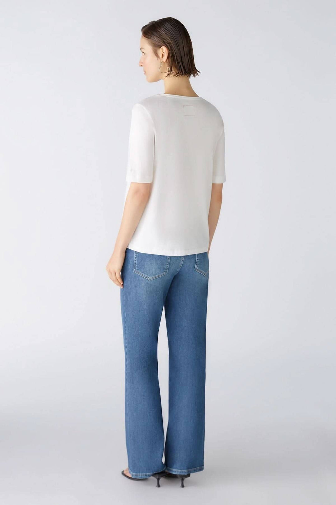 Femme vue de dos portant un t-shirt blanc, jeans larges, avec un fond neutre.