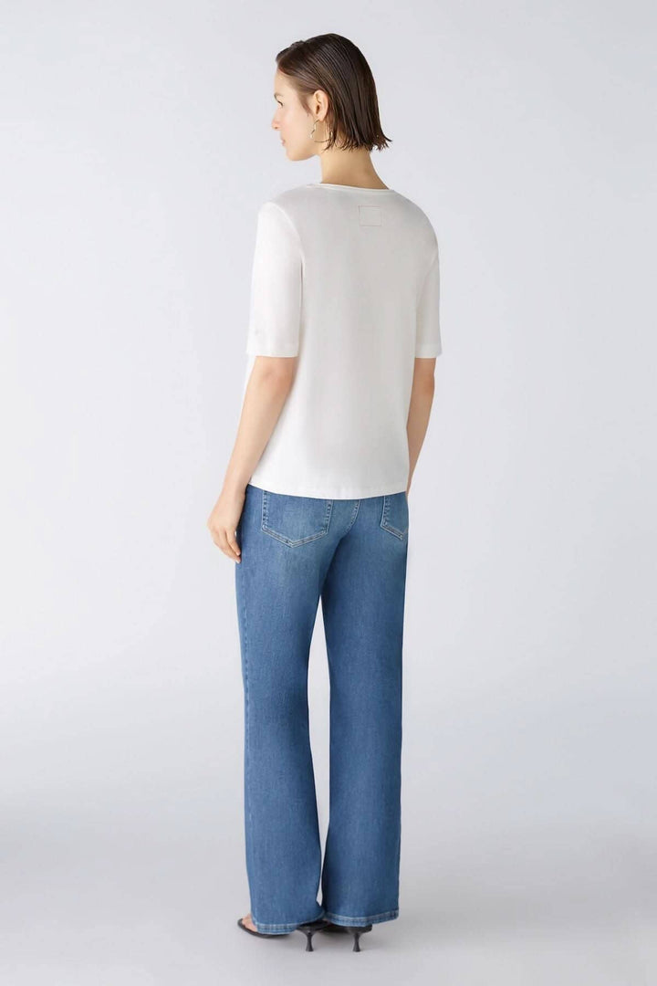 Femme vue de dos portant un t-shirt blanc, jeans larges, avec un fond neutre.