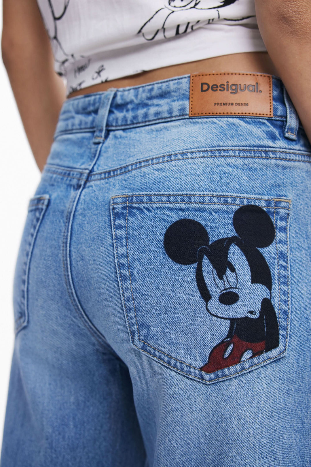 Jean à jambe large bleu avec broderie de Mickey Mouse sur la poche arrière, style décontracté et moderne.
