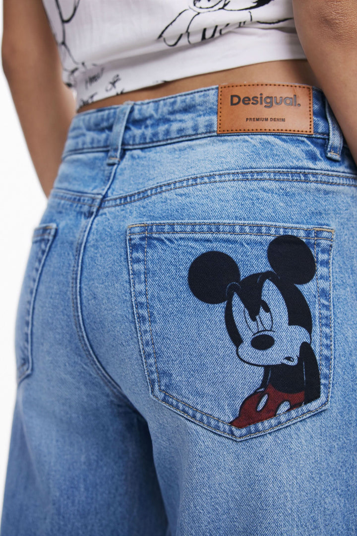Jean à jambe large bleu avec broderie de Mickey Mouse sur la poche arrière, style décontracté et moderne.